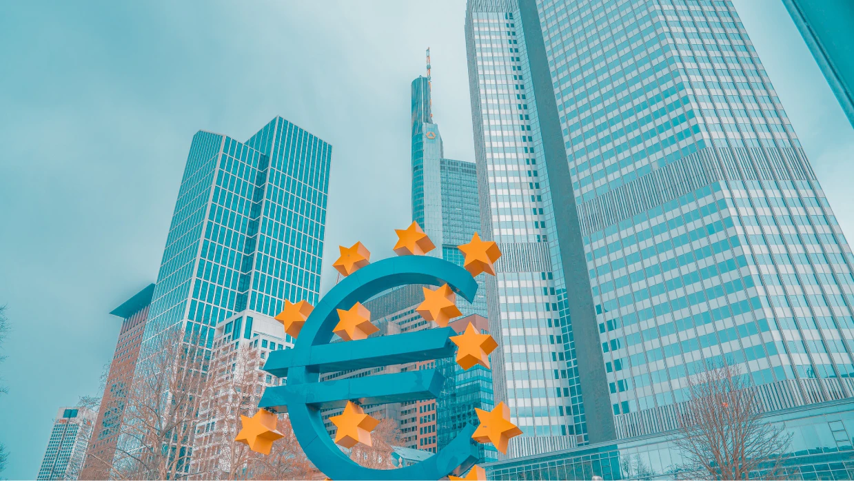 Foto eines Euro-Symbols mit Europa-Sternen vor Hochhäusern